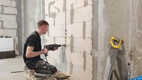 Man drills wall in construction site for electrical work in unfinished building Stock Footage 328443089