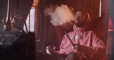 Man with drink and hookah in front of TV Stock Footage 229484959