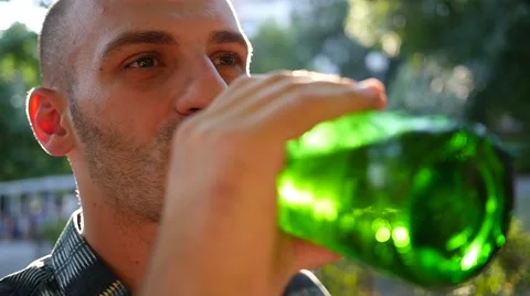 Man drinking alcohol beer from bottle outdoors in park in sun back light haze Stock Footage 65971015
