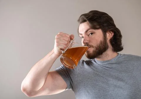 Man drinking beer with a big mug on a gray background, looking at camera Stock Photos