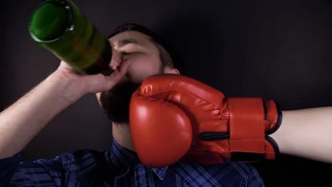 A man drinking beer from a bottle. A punch in the face with a red boxing glov Stock Footage 106350836