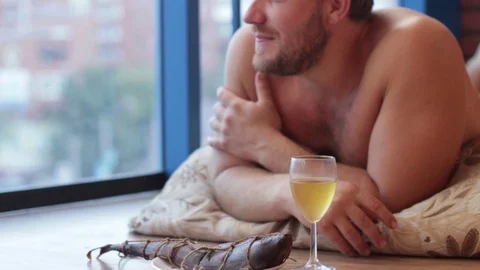 Man drinking beer from a glass and eat fish, lying on the floor Stock Footage 70866837