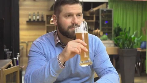 Man drinking beer looking to camera, smiling, portrait, in pub, cafe, steadicam. 库存影片 73067045