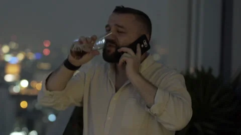 Man drinking beer on the rooftop at night and speaking on cellphone Stock Footage 93232078