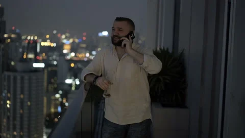 Man drinking beer on the terrace at night and speaking on cellphone Video stock 90551666