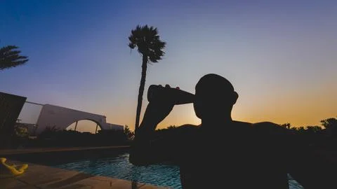 A man is drinking a beer while looking at the sky. silhouette against light Stock Photos