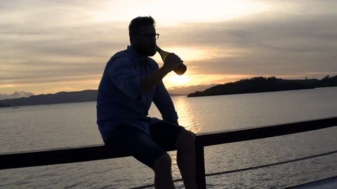 Man drinking beer while sitting on balustrade during sunset, steadycam shot, slo Stock Footage 83664959