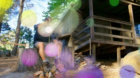 Man drinking bottle on stump after splitting wood, bokeh overlays drifting Stock Footage 333494696
