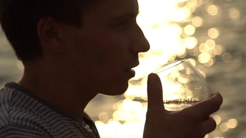 Man drinking bottle of wine during sunset near sea, slow  motion Video stock 80599054