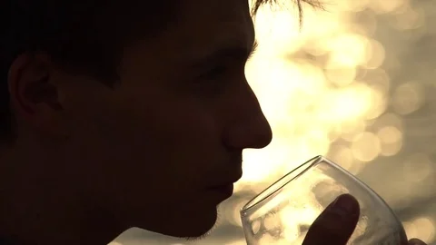 Man drinking bottle of wine during sunset near sea, slow motion Stock Footage