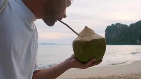 Man drinking coconut water drink with a straw on sandy tropical Railay beach Stock Footage 280940993