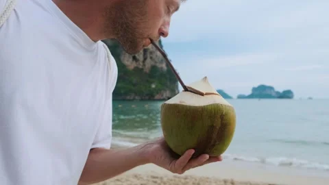 Man drinking coconut water drink with a straw on sandy tropical Railay beach Stock Footage 282919973