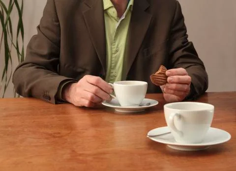Man drinking coffee and eating cookie at desk Foto stock