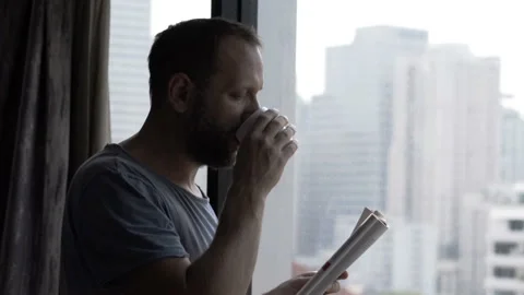 Man drinking coffee and reading newspaper in his apartment Stock Footage 93222627