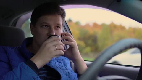A man is drinking coffee and talking on his mobile phone while driving a car. Stock Footage 81233522