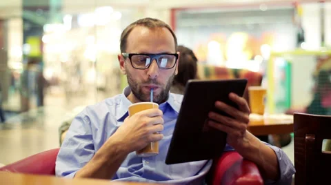Man drinking coffee and using tablet in the shopping mall cafe Stock Footage 37025942