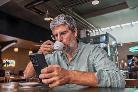 Man drinking coffee and using smartphone in cafe Stock Photos