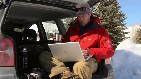 Man drinking coffee and working on laptop while sitting in back of car Vídeo Stock 935618