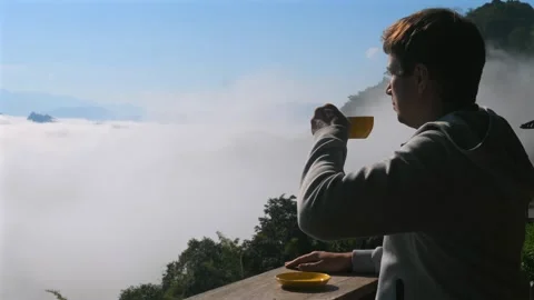 Man drinking coffee on balcony overlooking scenic mountain view with Stock Footage 276178617