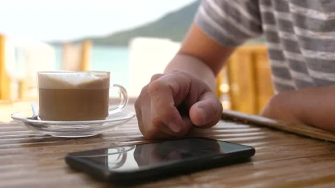 Man drinking coffee in beach cafe with sea view and uses phone. Video stock 199610463