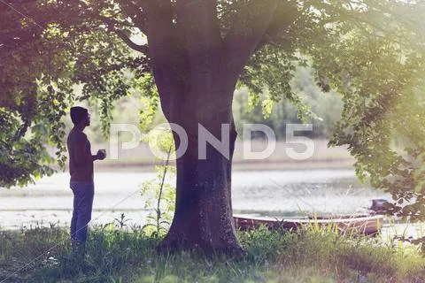 Man drinking coffee below tree at idyllic lakeside Stock Photos