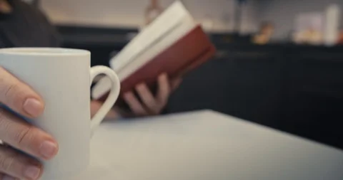 Man is drinking coffee or tea while reading a book in kitchen Stock Footage 100592053