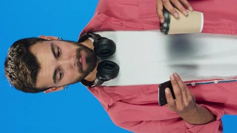 Man drinking coffee from paper cup on blue background and looking at phone. Stock Footage 143906880