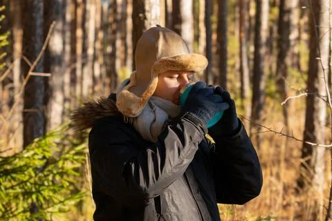 Man drinking coffee from thermos during weekend hiking in winter forest. Ba.. Stock Photos