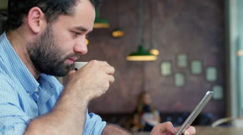 Man drinking coffee in trendy coffee shop, while checking his tablet Stock Footage 63018689