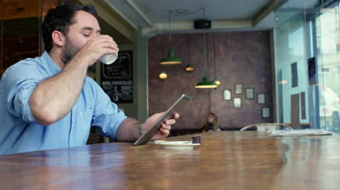 Man drinking coffee in trendy coffee shop, while checking his tablet Video stock 63023941