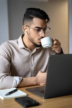Man drinking coffee watching webinar using laptop sitting at desk in home office Stock Photos