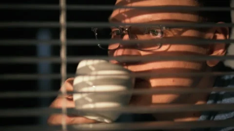 Man drinking coffee while looking through blinds in a cozy room during morni Stock Footage 304277656