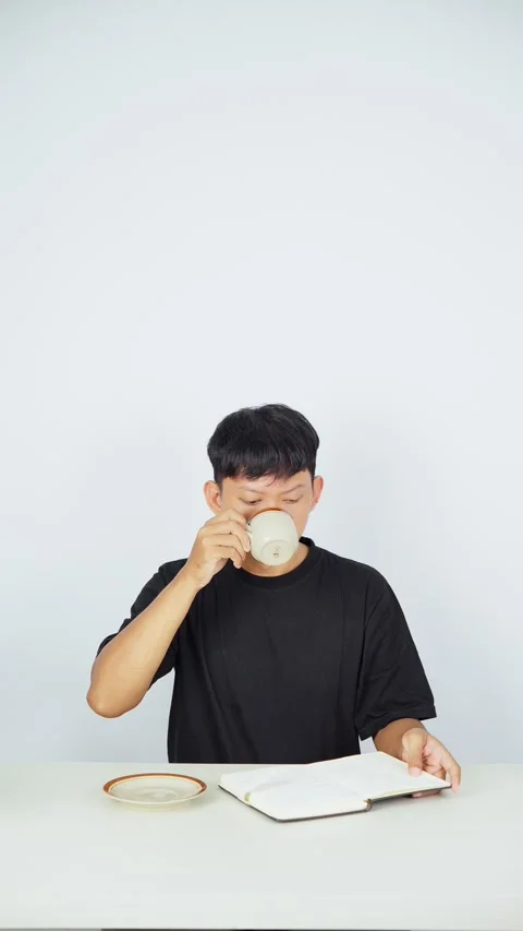Man Drinking Coffee While Reading Notebook on White Background 스톡 동영상 347105523