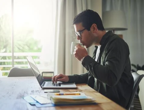 Man drinking coffee while working on laptop at home Stock Photos