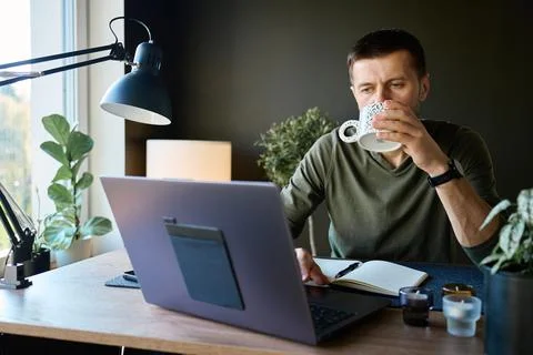 Man drinking coffee while working on laptop at table Foto stock