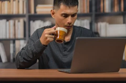 Man Drinking Coffee While Working on Laptop in a Cozy Library Setting Stock Photos