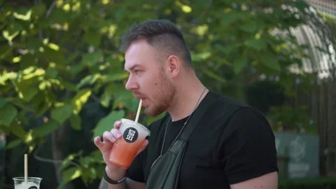 Man Drinking Cold Drink Cocktail Through Straw From Plastic Cap In Garden Video stock 155357513