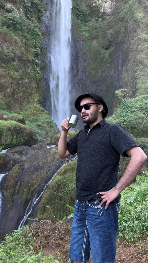 Man Drinking from Cup by Waterfall in Green Forest Vertical Shot Stock Footage 323913434
