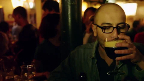 Man Drinking Dark Stout Beer from Glass inside Crowded Bar 库存影片 347188956