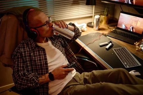 Man Drinking Energy Drink While Playing Video Games at Computer Desk Фото