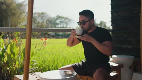 Man Drinking Fresh Morning Coffee Enjoying a Peaceful Rice Field View in Bali Stock Footage 345038924