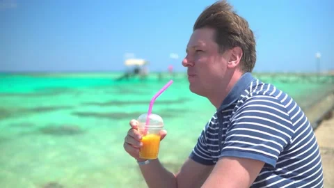 Man drinking fruit cocktail by the azure sea Stock Footage 152858791