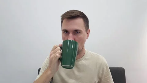 Man drinking from green ceramic mug while seated on a grey chair Stock Footage 284042973