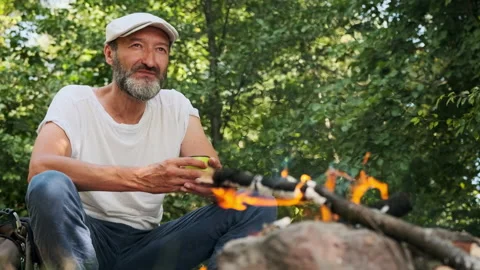 A man is drinking hot tea by the fire in the forest. In summer, Stock Footage 148339128