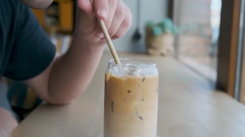Man drinking iced latte coffee in a glass with a straw in coffee shop. Cold Video stock 249663240