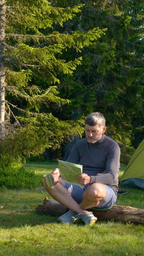 Man Drinking From Metal Mug While Reading Map At Forest Campsite Stock Footage 335129683