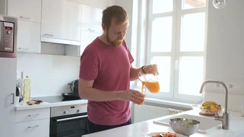 Man drinking orange juice in a white light kitchen Stock Footage 138751297