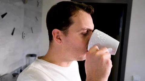 A man drinking pensively from a white cup at home in the kitchen Video stock 168572074
