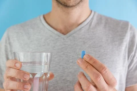 Man drinking a PrEP blue pill with glass of water. HIV prevention using Pre Foto stock