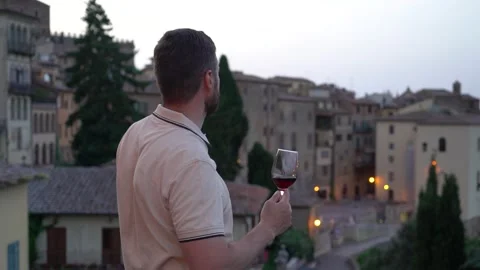 Man drinking red wine and looking at ancient italian city at the evening Stock Footage 245091823